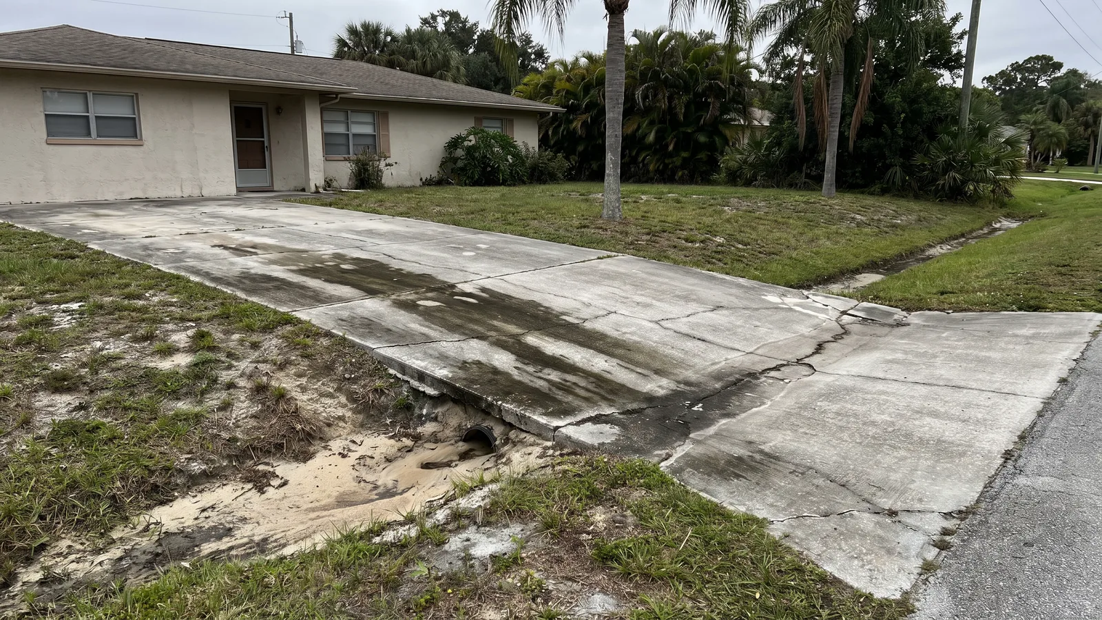 Older Florida driveway cracked and sunken where sandy base washed out beside a swale